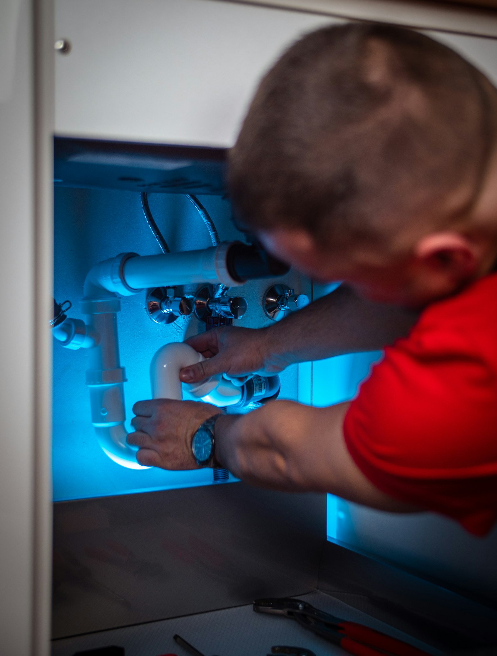 Plumber working on pipes inside a cabinet